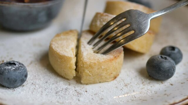 Metal fork and knife cutting and stringing delicious cheese pancake piece cowered with sugar powder extreme closeup slow motion