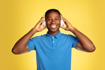 Music in headphones. Young african-american man's portrait isolated on yellow studio background, facial expression. Beautiful male portrait with copyspace. Concept of human emotions, facial expression