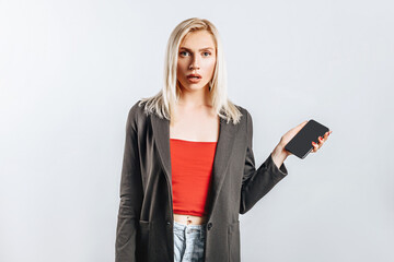 Fototapeta premium Beautiful young girl unhappy and holding phone on gray isolated background