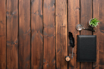 Black leather book, magnifying glass and quill pen on the brown wooden desk flat lay background with copy space.