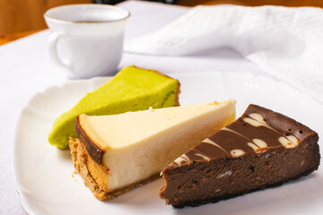 Set of New York, chocolate and pistachio cheesecake on white plate and cup of coffee