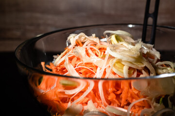Healthy salad with carrot and leek in transparent bowl on dark background