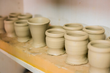 Crafting, DIY, artwork and handmade concept. Unfinished mugs in row on shelf of pottery workshop, ceramic studio - close up view