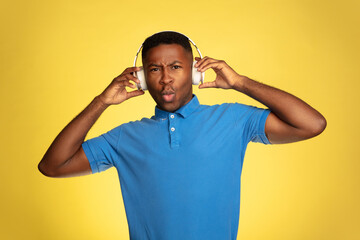 Fototapeta na wymiar Music in headphones. Young african-american man's portrait isolated on yellow studio background, facial expression. Beautiful male portrait with copyspace. Concept of human emotions, facial expression