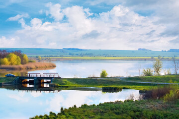 Spring landscape with river and high sky with big white cloud in good weather, bridge over the river