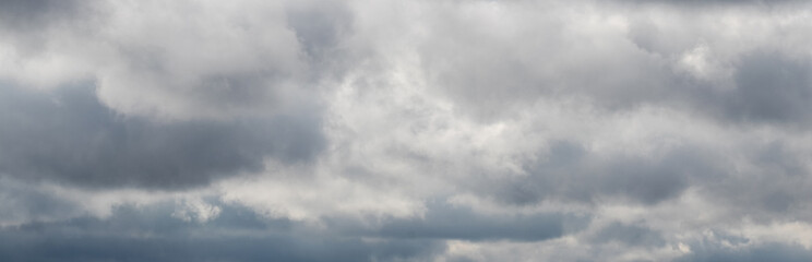 Cloudy sky with gray clouds and a light gap in the center, panorama of the sky