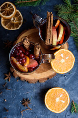 wo glasses of hot red mulled wine decorated with orange, clove, cinnamon and anise. Christmas lights on background. Rustic decor, cozy atmosphere, festive mood.