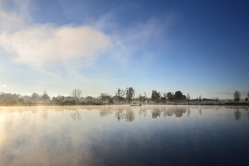 Landscape with a lake in autumn, over which the fog clears in the morning and the sun rises