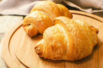 Freshly baked croissants on wooden cutting board, top view