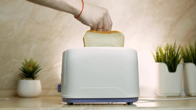 a man's hand loads two pieces of white bread into a toaster on the table.