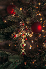 Gold and red cross ornament hanging on a Christmas tree branch