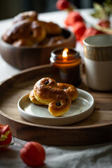 Two Swedish saffron buns (lussekatter), lit  candle and cup of coffee on wooden tray.