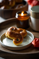 Two Swedish saffron buns (lussekatter), lit  candle and cup of coffee on wooden tray.