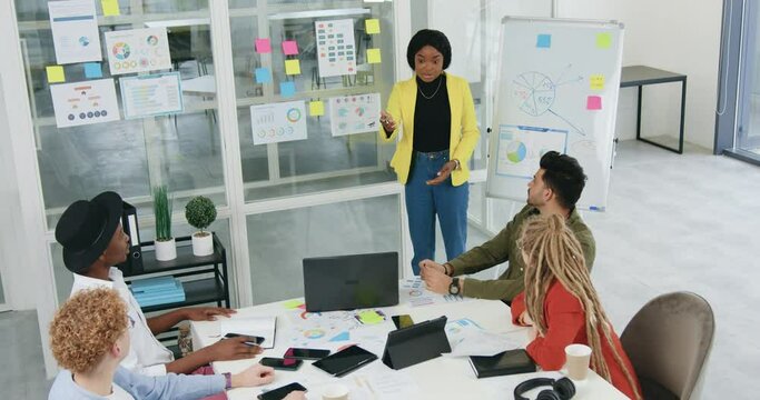 Top view of pretty smiling emotional motivated black-skinned woman which discussing with her concentrated creative mixed race subordinates the concept of business strategy in project using