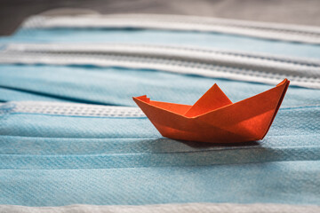 Orange origami boat sailing on a blue sea made with surgical masks.Pandemic problems concept, origami ship with surgical masks.