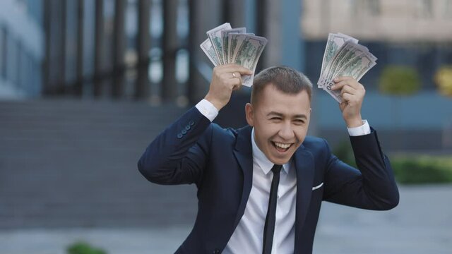 Man shows money and celebrating success while looking to camera. Amazed happy excited businessman with money - U.S. currency dollars banknotes