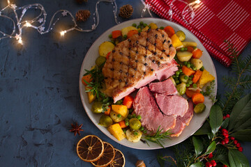 Roasted sliced ham with vegetables. Christmas decorations. New Year dinner table. View from above, top studio shot