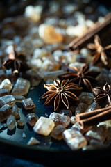 Close up brown sugar crystals, anise stars and cinnamon sticks on deep blue background.