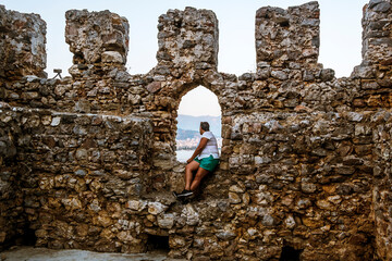 A girl sits on the wall of the medieval fortress of Alanya in Turkey at sunset