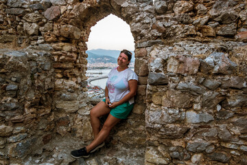 A girl sits on the wall of the medieval fortress of Alanya in Turkey at sunset