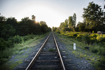 Railway station against beautiful sky at sunset. Industrial landscape with railroad, colorful sky with clouds, sun, trees and green grass.