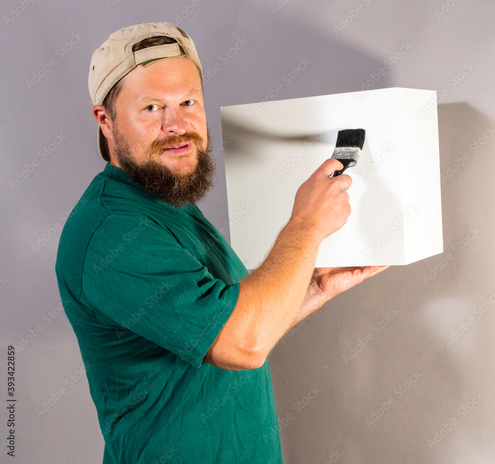 Wall mural joyful bearded foreman in green t-shirt with brush and blanc object looks like cube