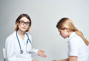 Doctor sits on a chair and woman patient indoors on a light background cropped view