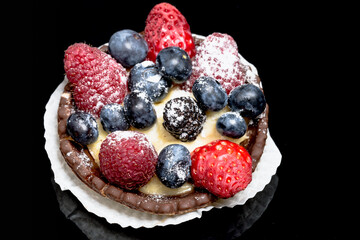 Tartelette mit Himbeeren, Blaubeeren und Erdbeeren vor einem schwarzem Hintergrund
