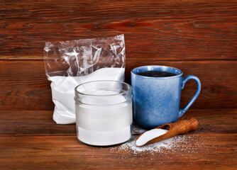 Fructose in a transparent pack with cup of tea, jar and scoop of sorbitol on a wooden background....