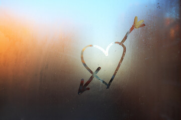 A heart with an arrow drawn on a fogged window against the city background. Heart on the fogged glass. Heart on the background of the window.The heart is a symbol of love drawn on glass.