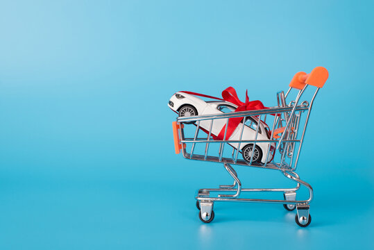 Sale concept. Close up photo of toy mini white car in miniature shopping cart isolated on blue background