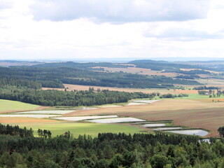 view of square water retention reservoirs in fields, cascades in agricultural landscape, forests and hills in background, summer
