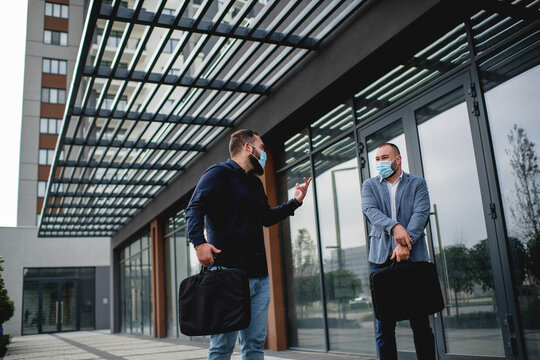 Two business people wearing protective face masks and talking to each outdoors
