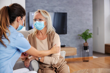 Senior woman with face mask sitting at home and listening advices from nurse during corona virus outbreak.