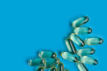 Transparent yellow pills of fish oil are scattered on one side against a light blue background. Blank for text about medicine, treatment or medicines.