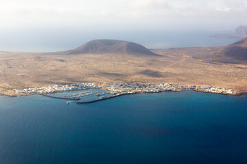 Ferry boat leaving La Graciosa island harbor to Lanzarote. Aerial view of volcanic landmark. Natural landscape by the sea