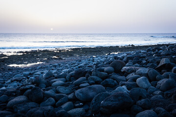 Obraz premium Sun goes down on horizon by sea on rocky beach in Lanzarote. Twilight on empty bay in Canary Islands