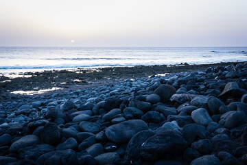Sun goes down on horizon by sea on rocky beach in Lanzarote. Twilight on empty bay in Canary Islands