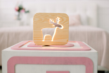 Front close up view of stylish wooden night lamp with deer picture, on pouf stool at cozy light...