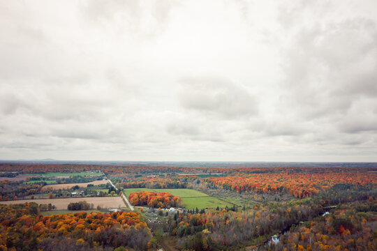 Beautiful fall aerial photograph of farm land and woods in upper Wisconsin during peak autumn colors with green tree leaves turning orange, yellow, and red and fluffy white clouds in the sky above.