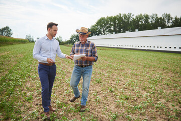 Farmer and businessman discussing data from clipboard on the field