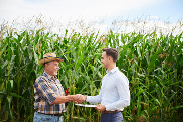 Farmer and businessman shaking hands at the cornfield