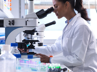 Female scientist examining a human sample on a glass slide under a microscope in the laboratory