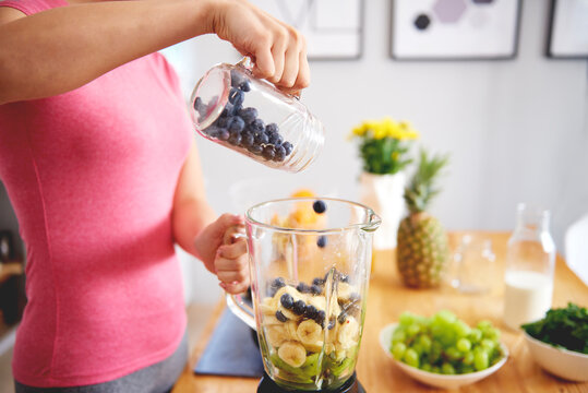 Young woman preparing smoothie in the kitchen, partial view