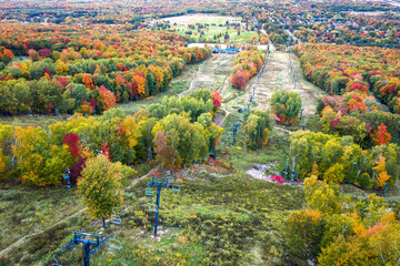 Beautiful aerial view looking down one of the ski runs at Rib Mountain in the autumn season with bright red, orange and yellow colored foliage on the trees lining the runs and chair lift.