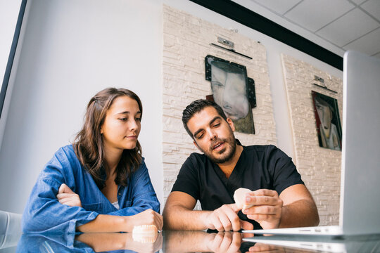 Handsome male dentist explaining female patient over gums model at desk in office