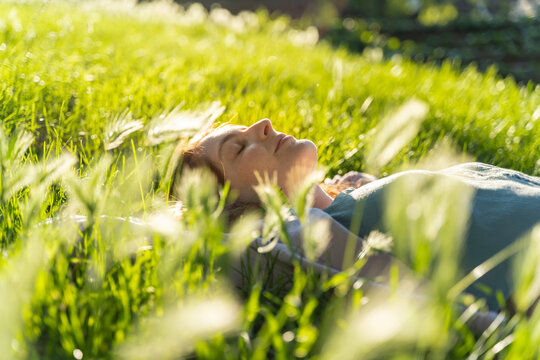 Young redheaded woman lying on meadow in a park