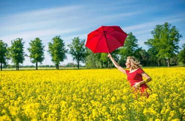 Happy woman holding red umbrella while standing amidst oilseed rapes