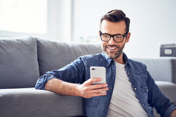 Smiling man in living room looking at cell phone