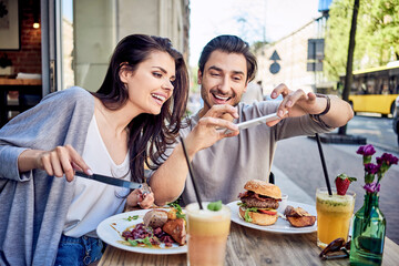 Happy young couple taking photo of food at outdoors restaurant